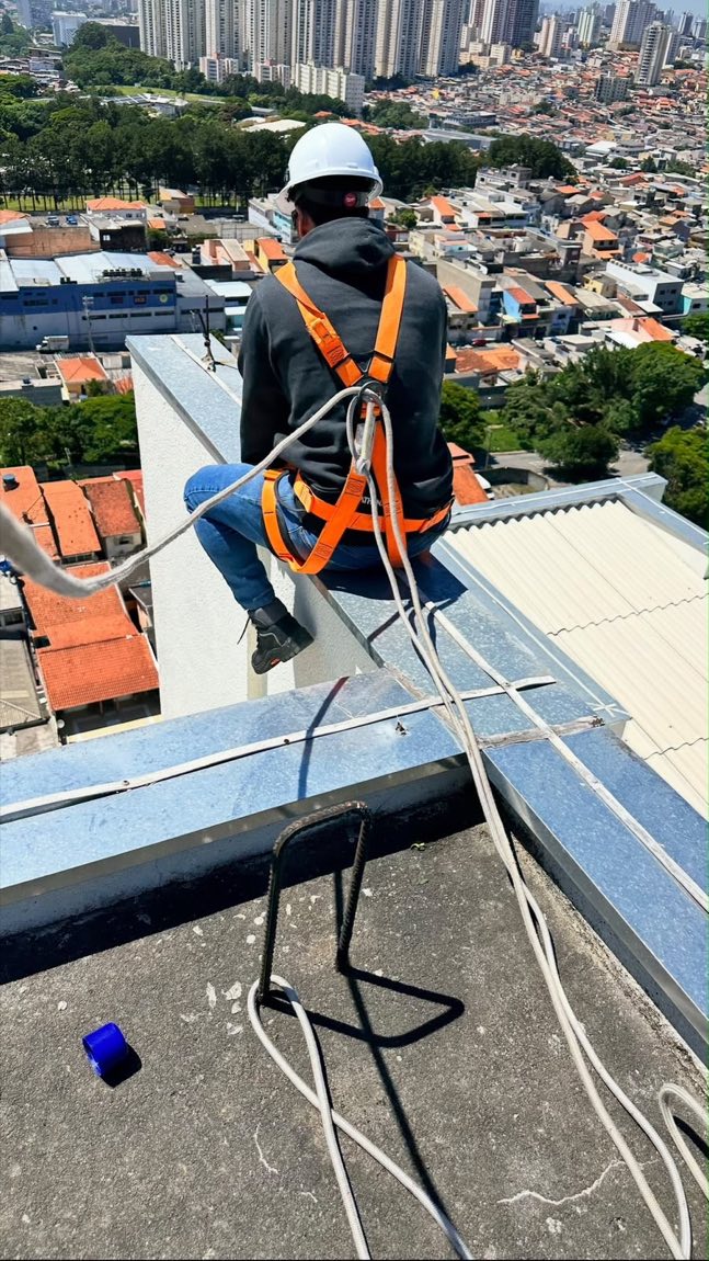 Profissional com cinto de segurança e capacete trabalhando na cobertura de um edifício