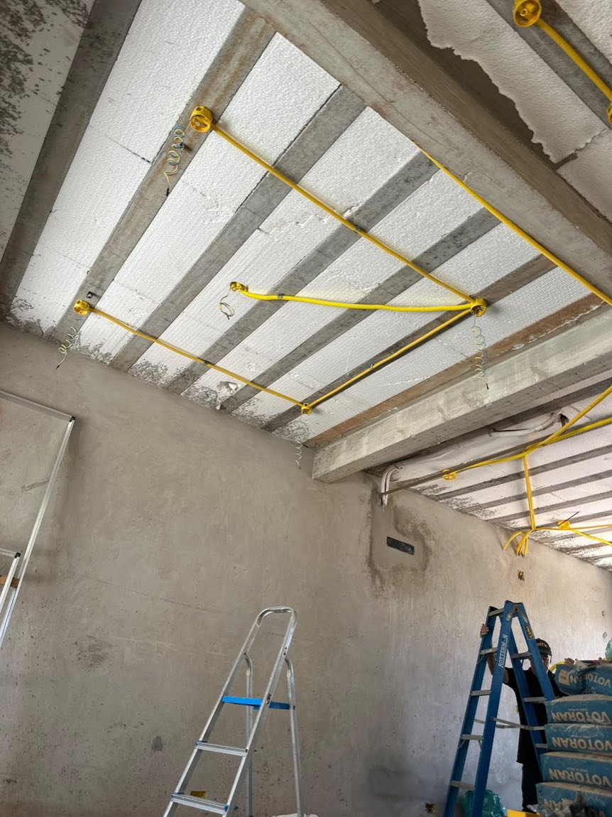Teto de obra com eletrodutos amarelos aparentes formando a infraestrutura elétrica