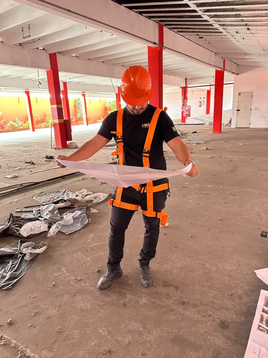 Profissional com capacete e cinto de segurança em obra comercial com colunas vermelhas